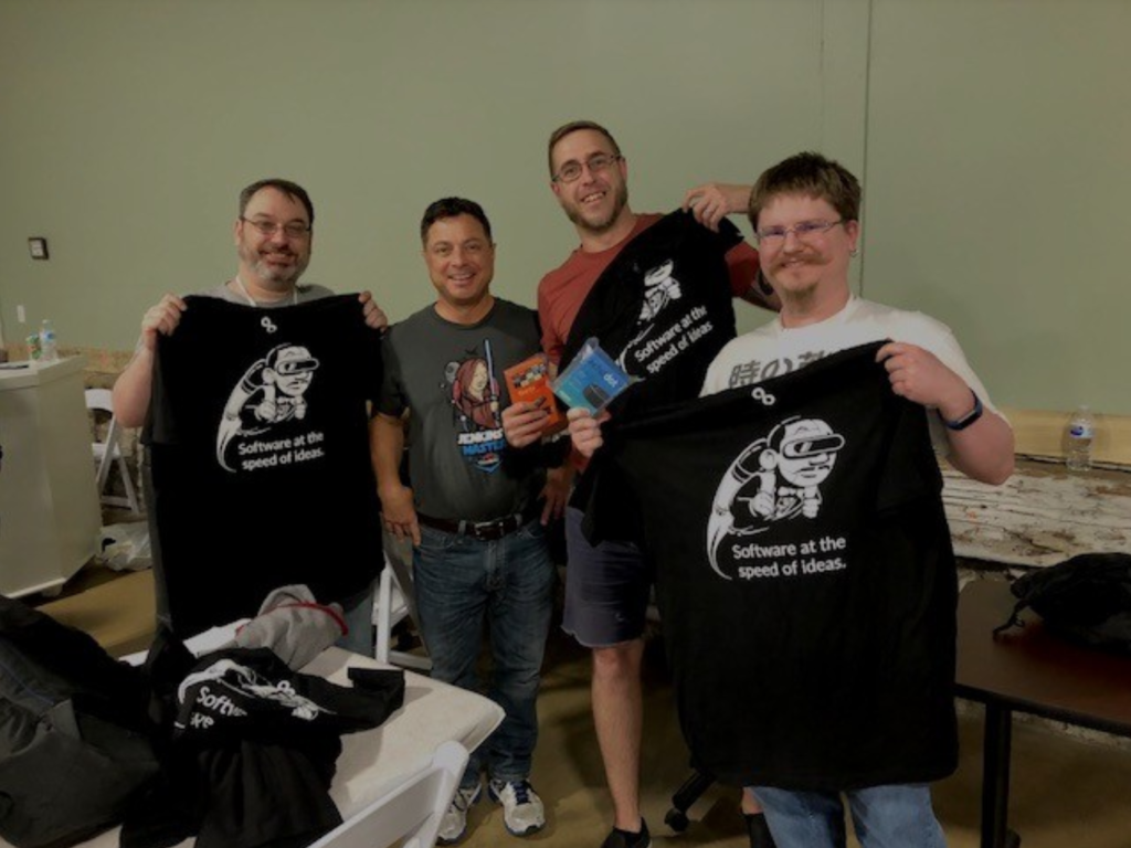 A group of 27Global software engineers hold up shirts in excitement.