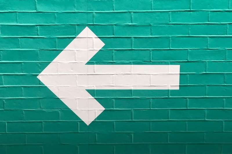 A white arrow on a green brick wall points to the left.